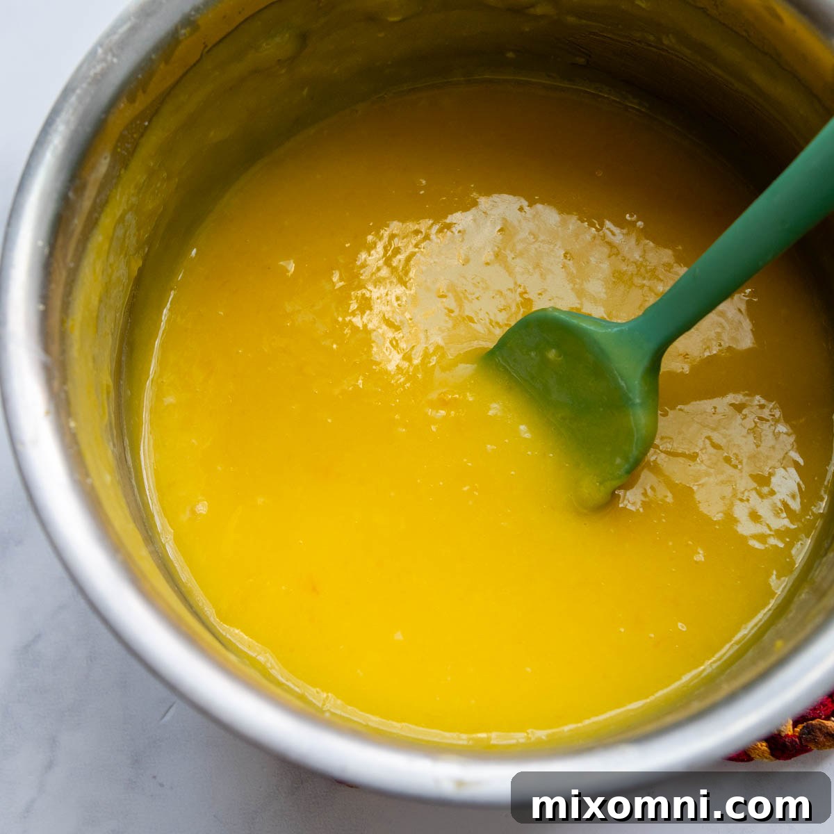 The lemon filling thickening in a saucepan with a spoon.