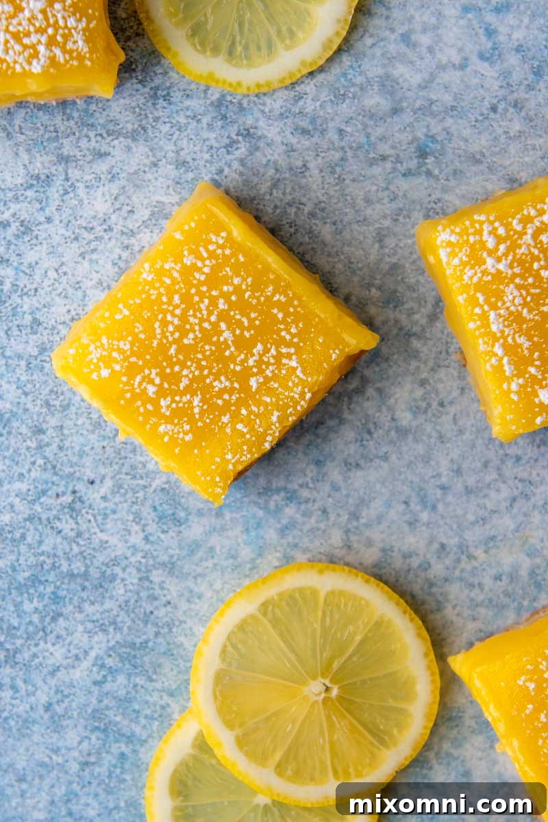 Overhead shot of cut lemon bars on a blue background with sliced lemons next to them.