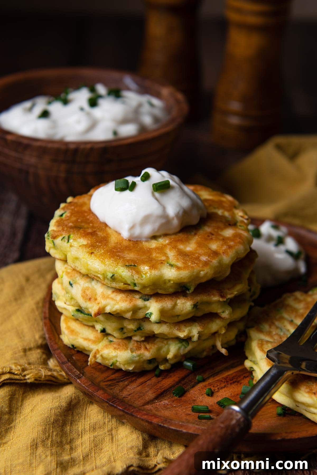 A stack of golden zucchini fritters presented on a elegant wood plate with a gold napkin underneath.