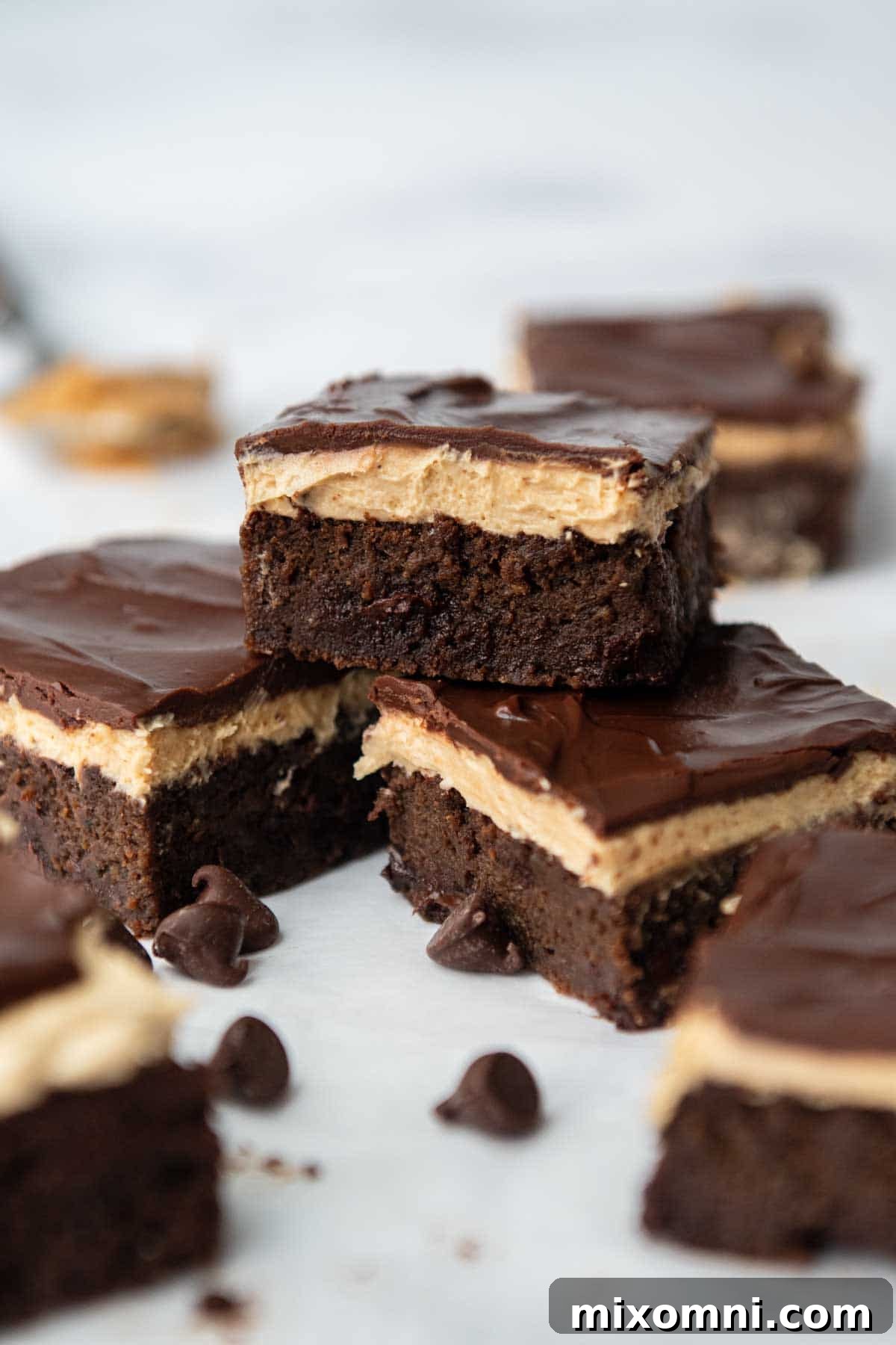 One rich zucchini brownie topped with fluffy peanut butter frosting, stacked on two others, surrounded by chocolate chips.