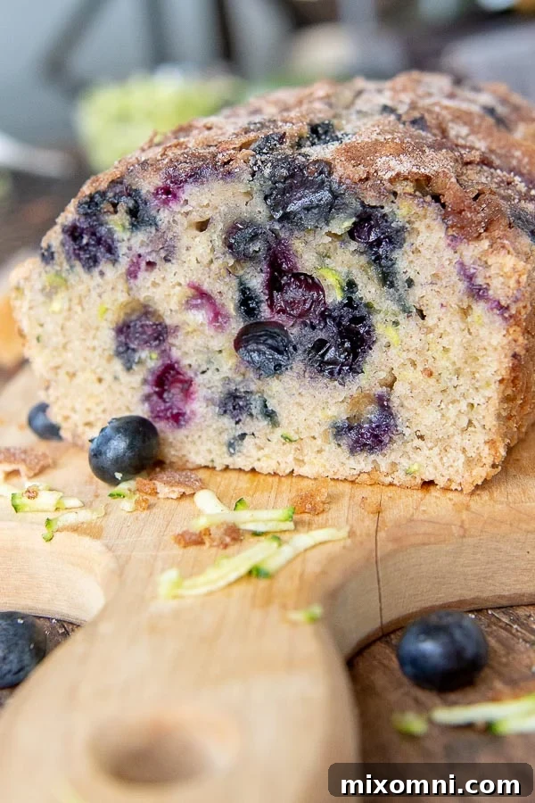 A delicious loaf of blueberry zucchini bread on a cutting board, with a slice already removed, highlighting the juicy blueberries.