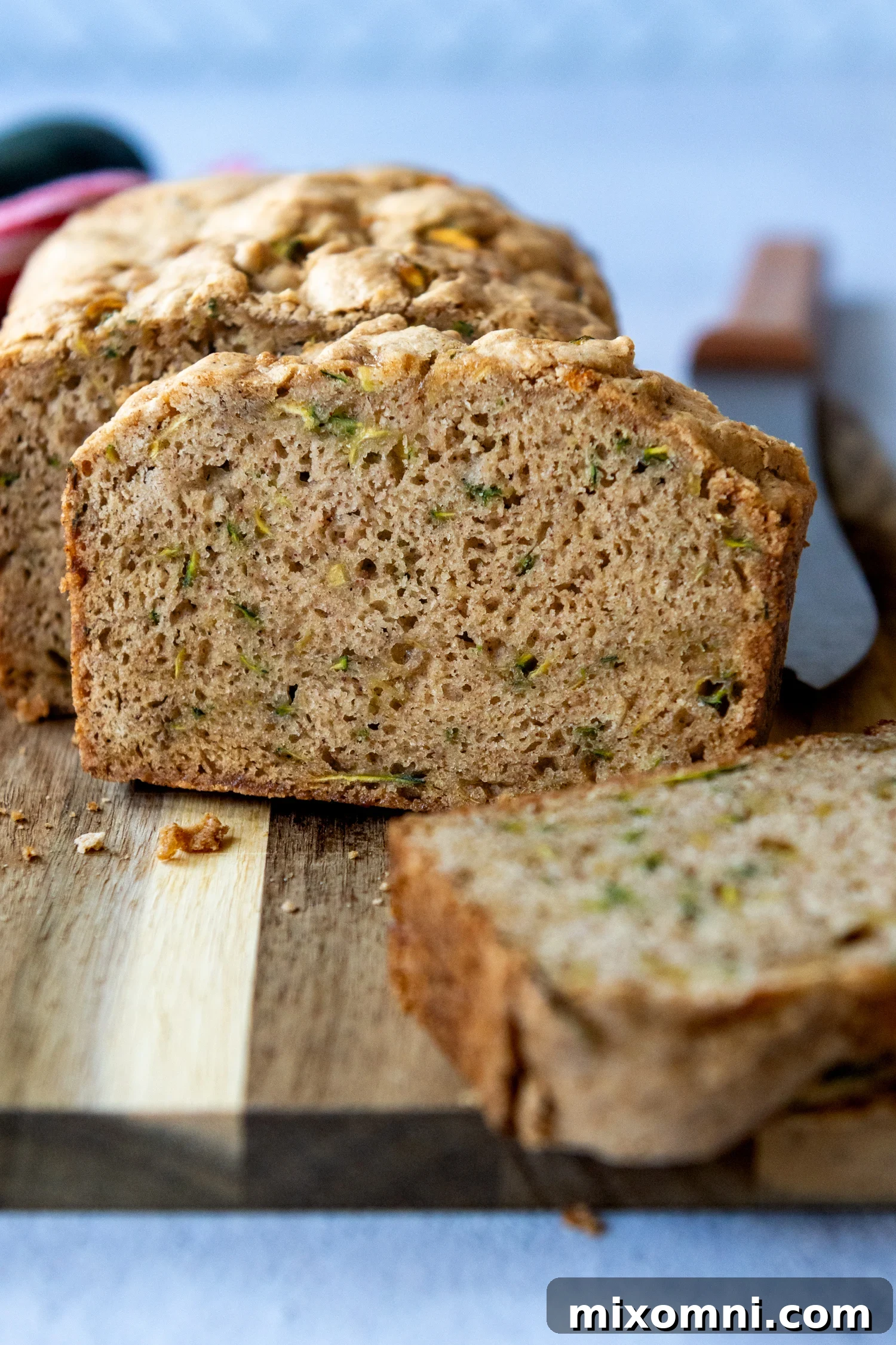 A perfectly baked slice of zucchini bread standing upright on a rustic wooden cutting board.