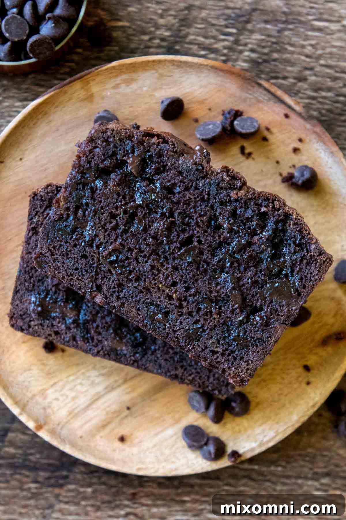 Two pieces of decadent chocolate zucchini bread, stacked on a wooden plate, tempting with their fudgy texture.