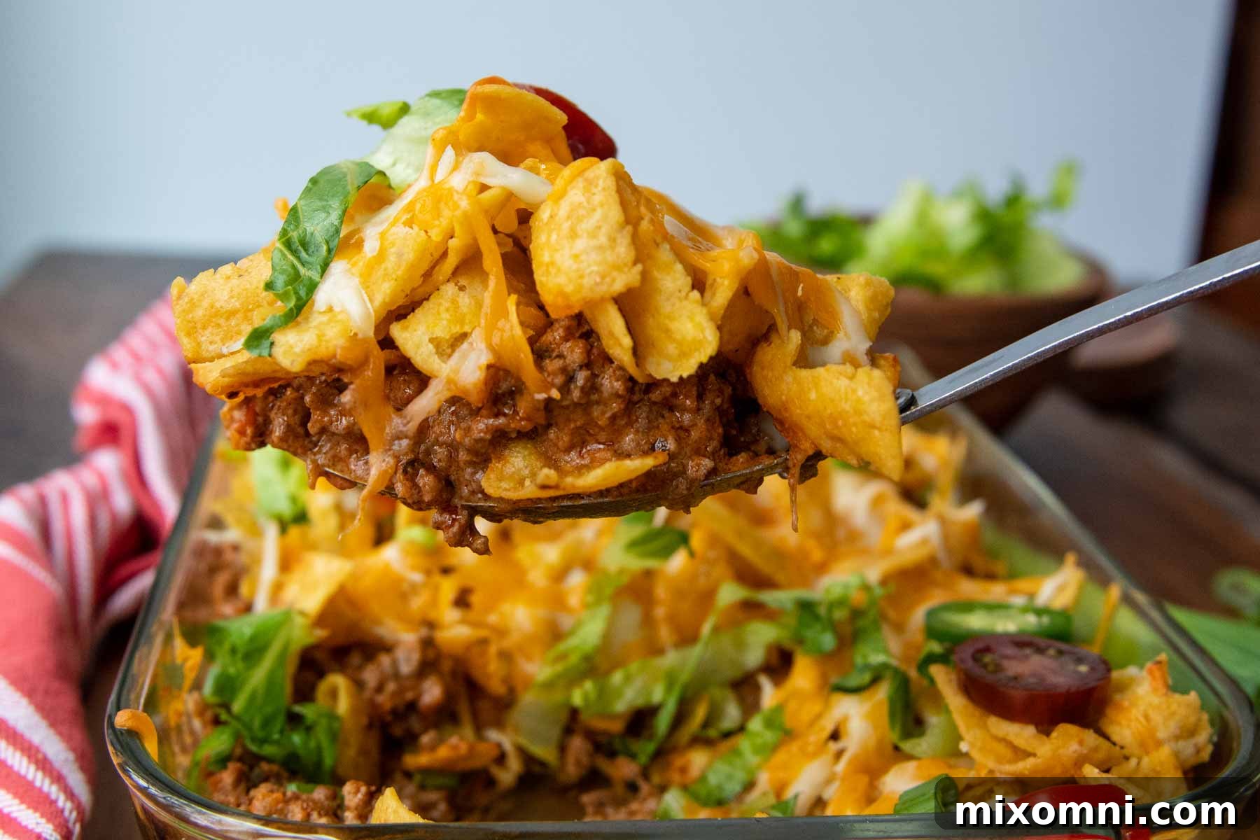 a spoon lifting out the walking taco bake out of a casserole dish
