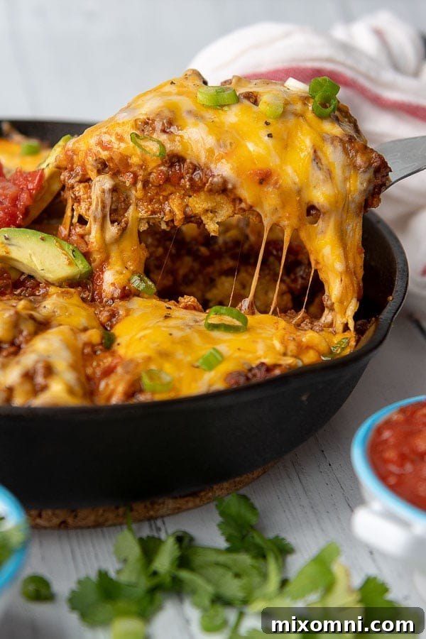 a slice of tamale pie being lifted out of a cast iron skillet with cheese stringing off
