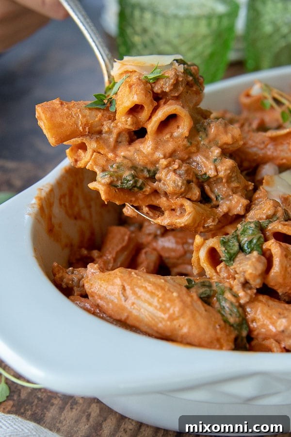 a serving spoon holding up a serving of pasta covered in sausage red sauce