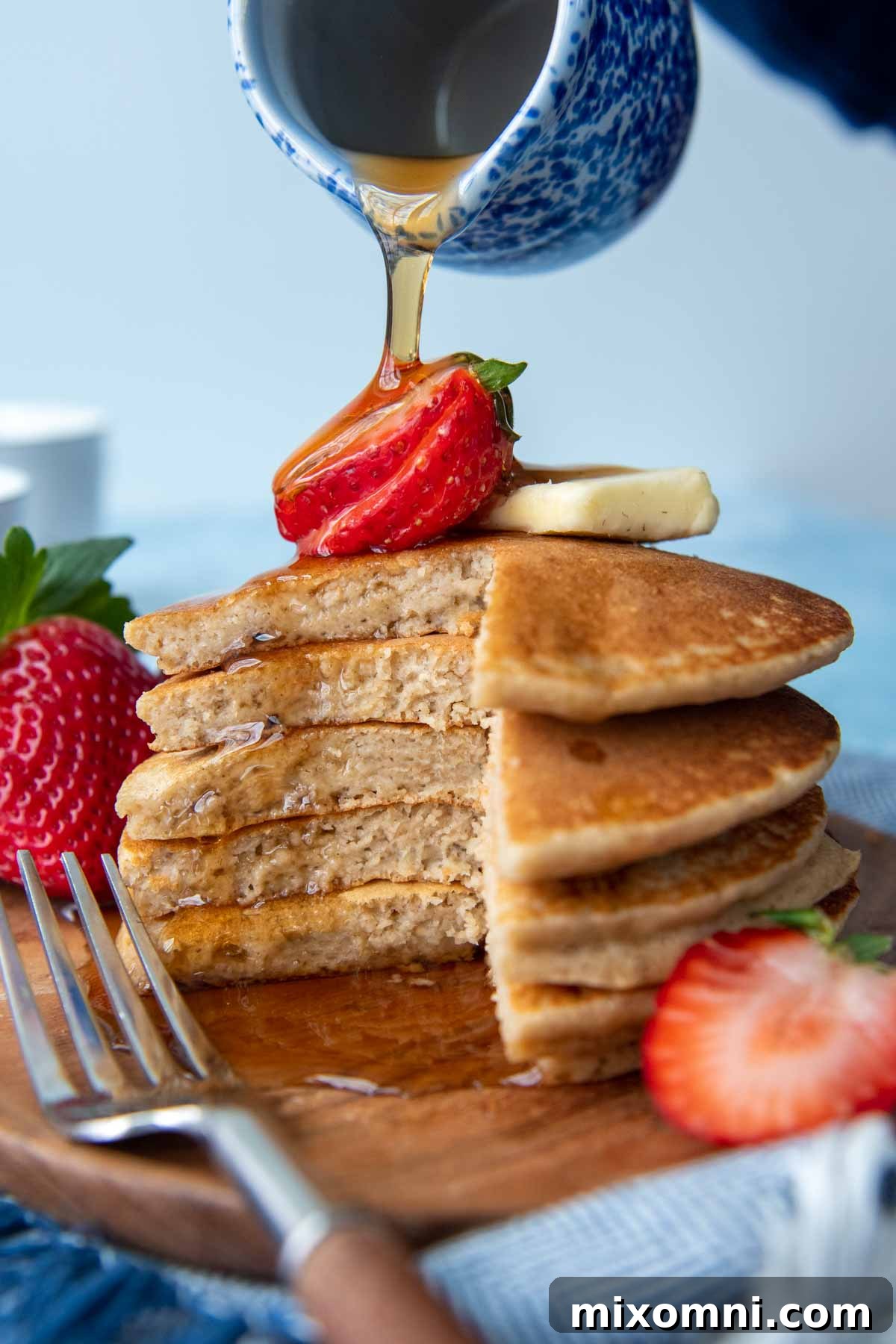 a stack of cut pancakes with a strawberry on top and syrup dripping down