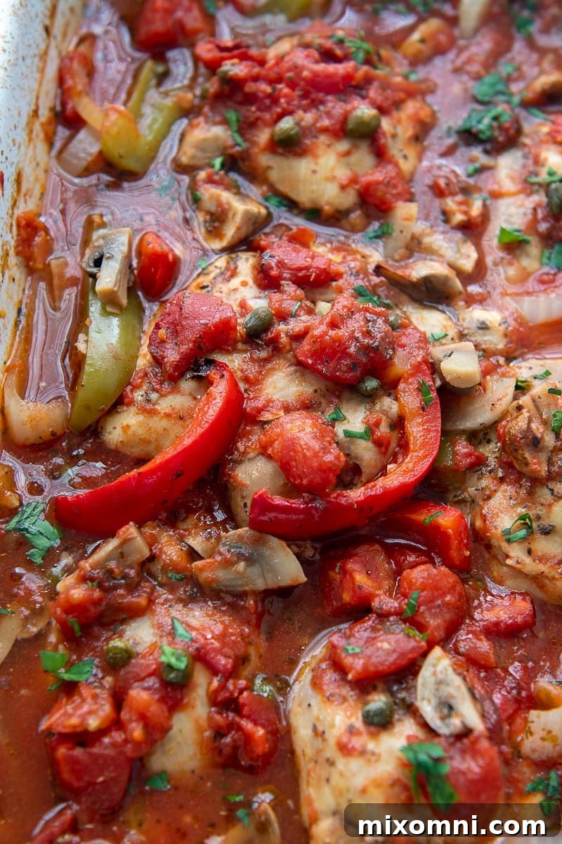 close up of baked chicken with peppers, mushrooms, and onions in a tomato sauce