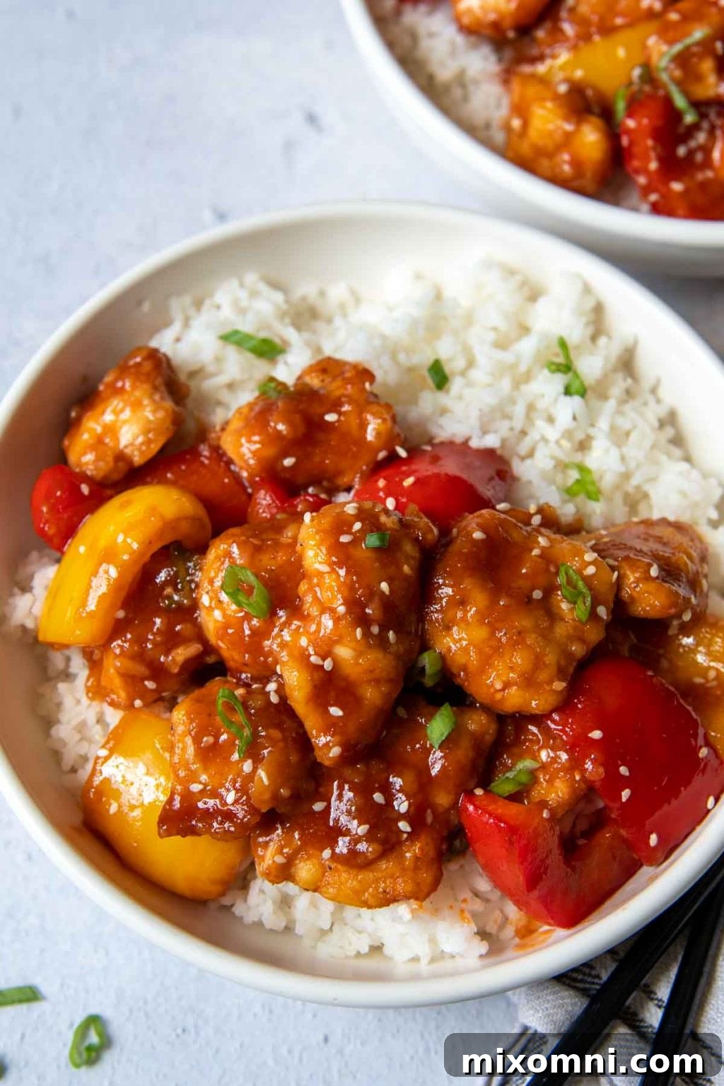 two bowls of sweet sour chicken with chopsticks laying next to it