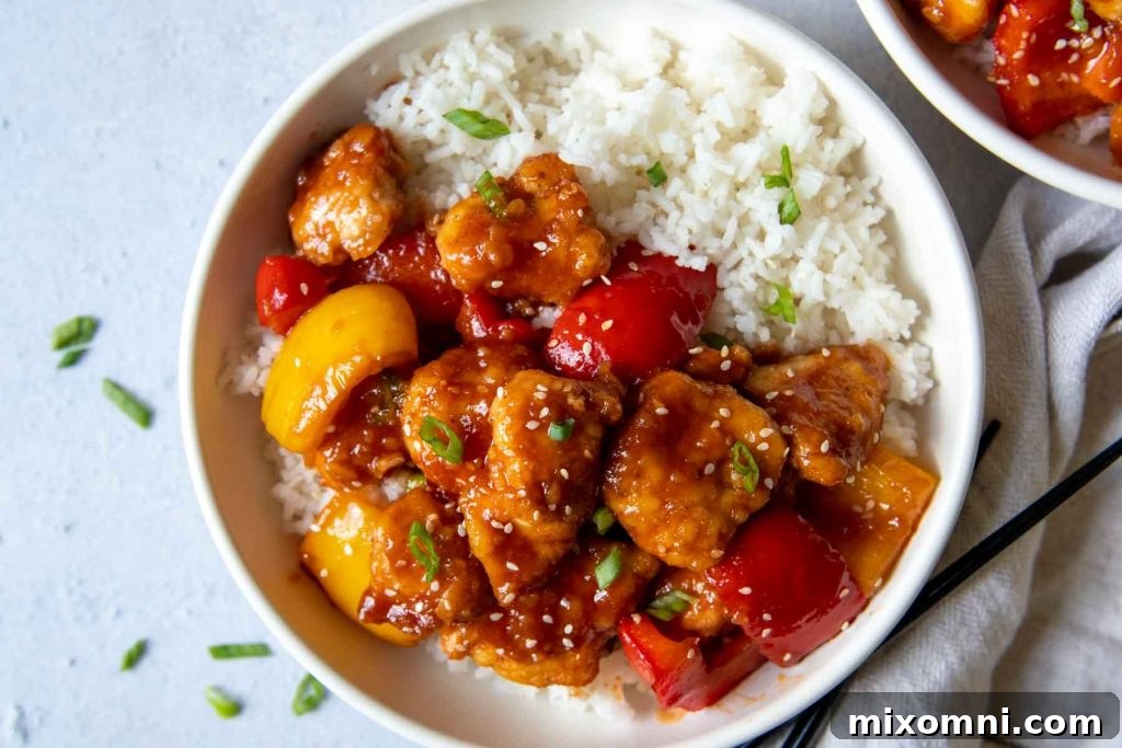 overhead shot of sweet and sour chicken in a white bowl with rice