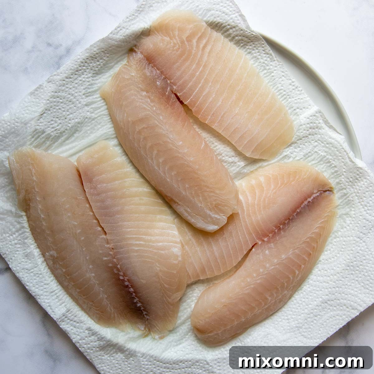 Fish fillets being patted dry with paper towels on a plate
