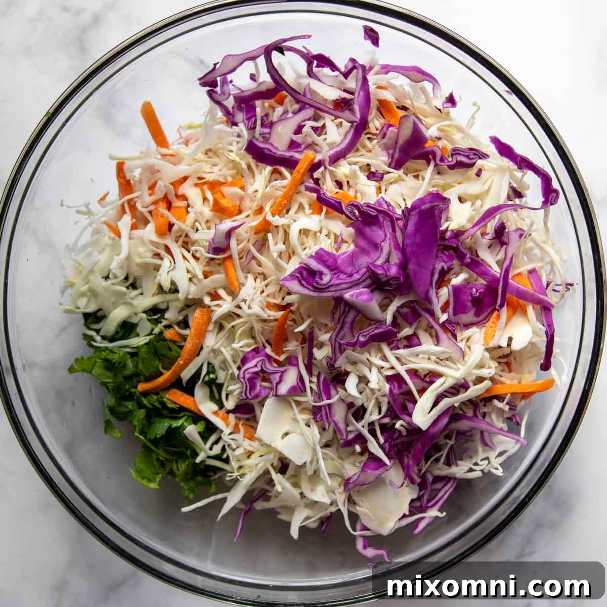 Coleslaw mix and cilantro combined in a glass bowl with the dressing