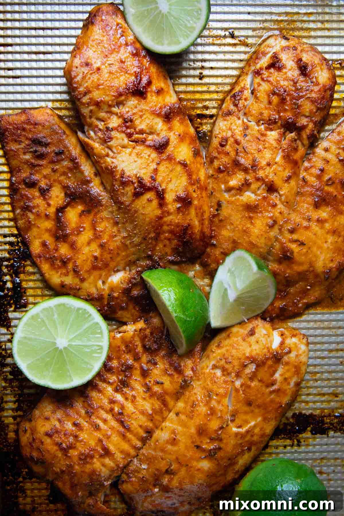 Baked blackened seasoned fish fillets on a baking sheet with lime wedges