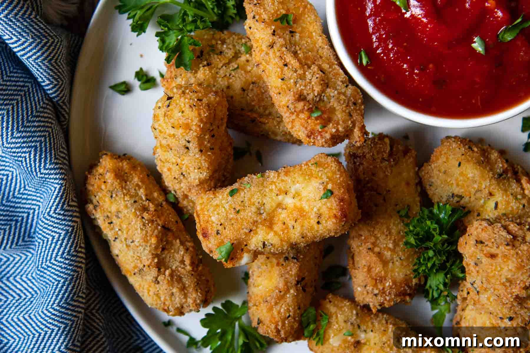 An overhead shot of crispy, golden-brown mozzarella sticks arranged neatly on a white plate, served with a side of marinara sauce.