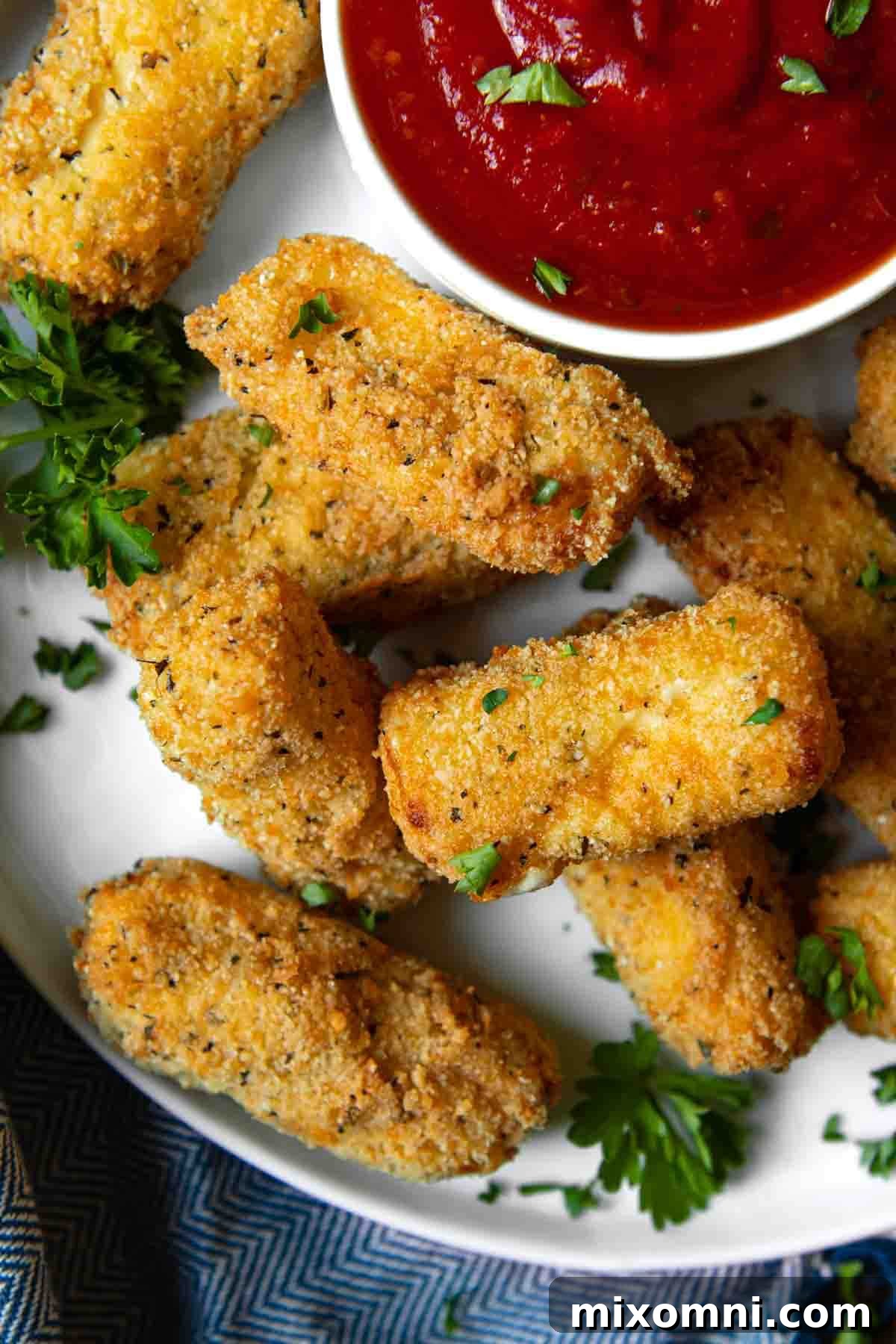 An overhead shot of a plate of perfectly golden, gluten-free mozzarella sticks, garnished with fresh parsley.