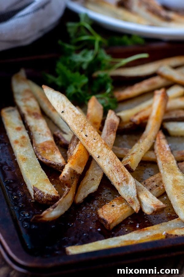 A close-up of golden, perfectly crispy oven fries spread out on a baking sheet, glistening with seasoning.
