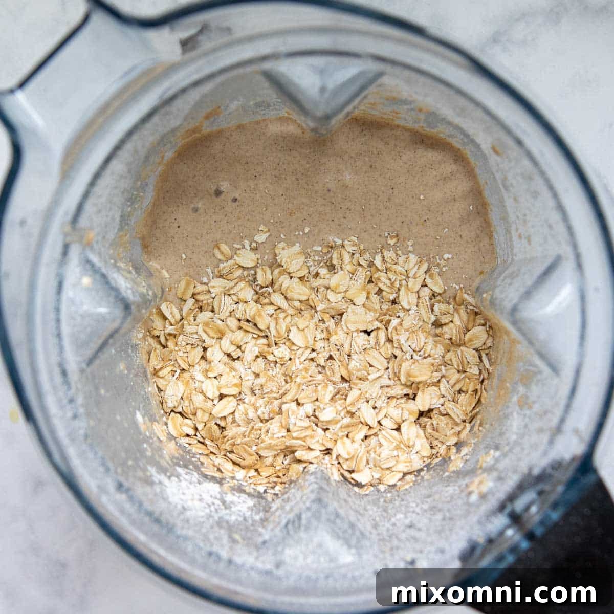 Remaining whole oats being added to the blended muffin batter in the blender, before final pulsing.