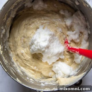 Egg whites being gently folded into banana cake batter to ensure a light and airy texture.