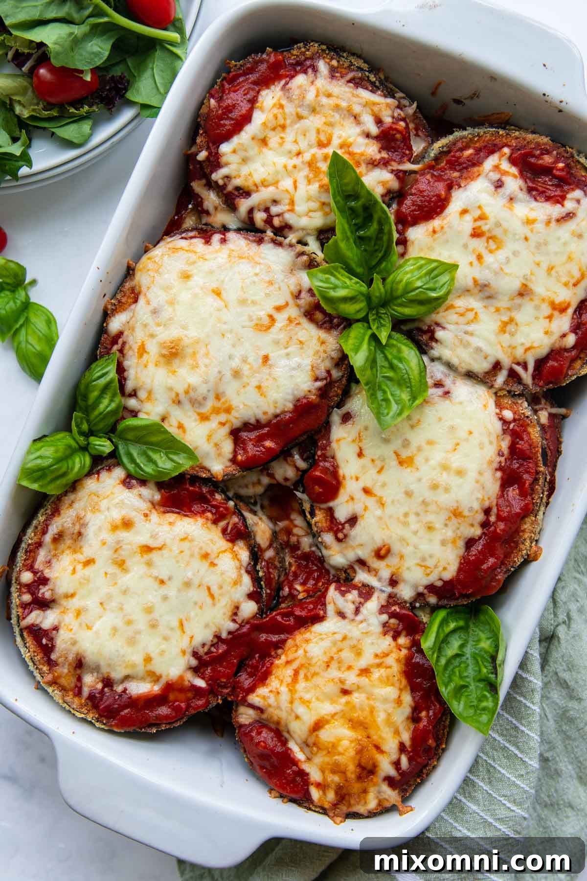overhead shot of eggplant parm in a white baking dish with a salad next to it
