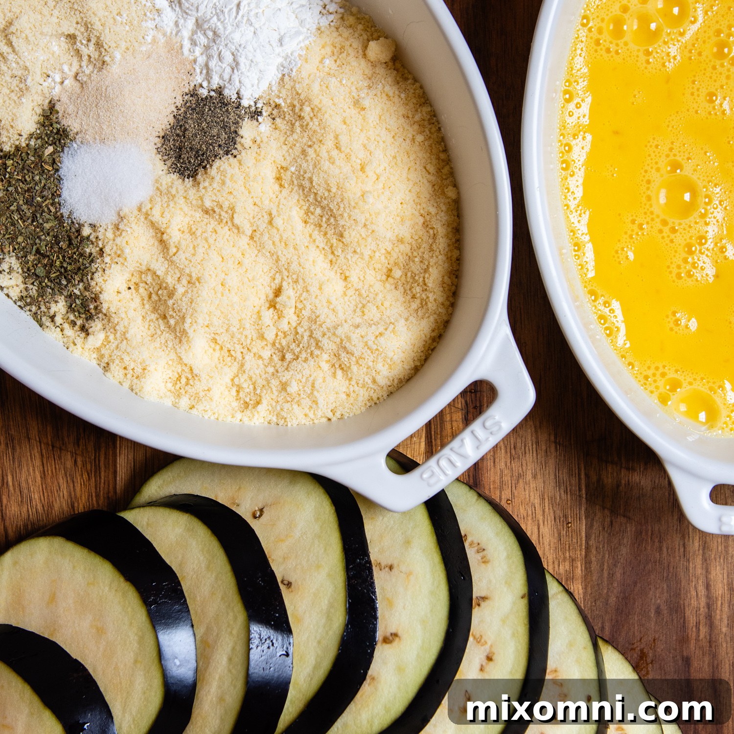 the almond flour breading station laid out with beaten eggs and sliced eggplant.