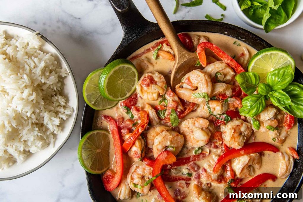 Horizontal shot of creamy coconut shrimp in a black skillet with a bowl of rice next to it, ready to serve.