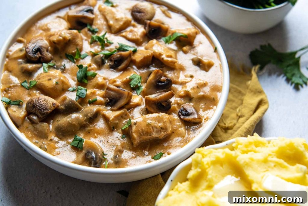 A close-up shot of creamy Instant Pot Chicken Stroganoff in a white bowl, garnished with fresh herbs and a gold napkin, highlighting its inviting texture.