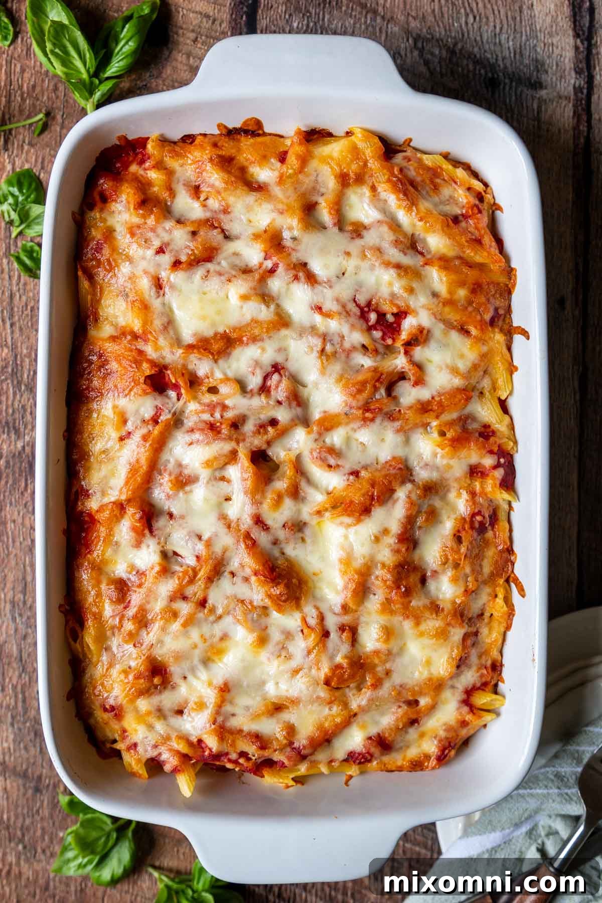 Overhead shot of golden brown baked ziti in a white baking dish, fresh from the oven, with melted cheese and bubbling sauce.