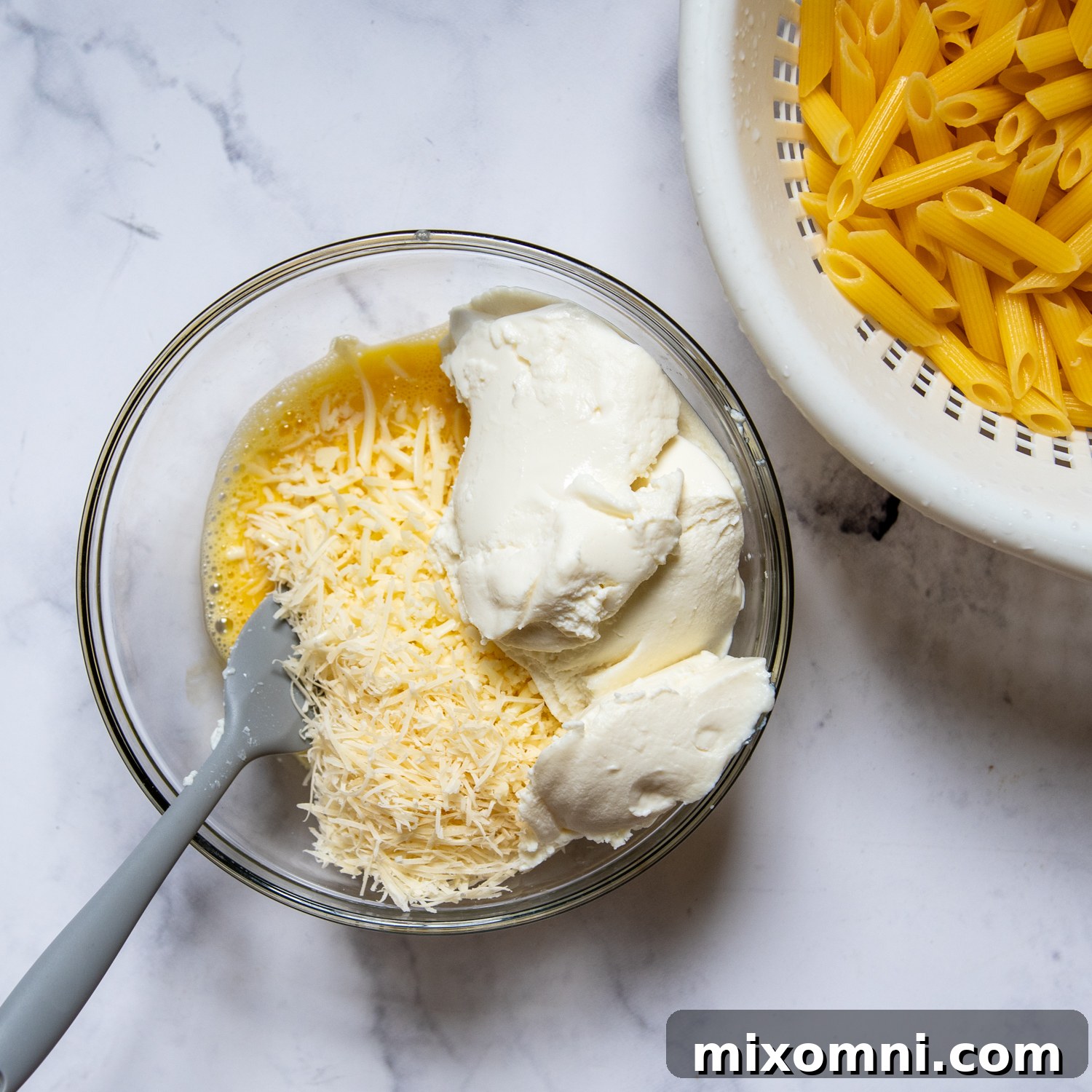 A bowl of creamy ricotta cheese filling next to a pot of cooked ziti pasta, ready for assembly.