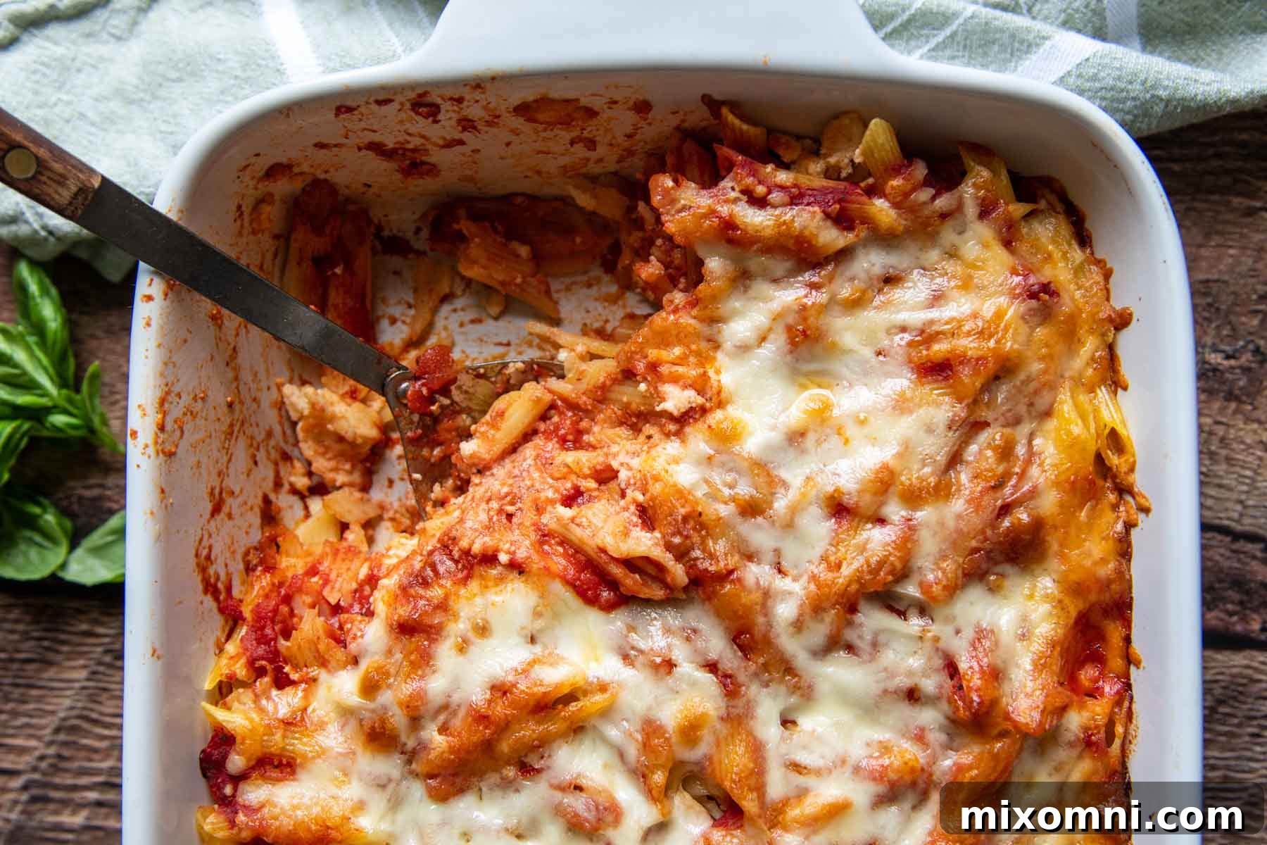 A spoon scooping a generous portion of meatless baked ziti from a casserole dish, revealing tender pasta, rich sauce, and melted cheese.