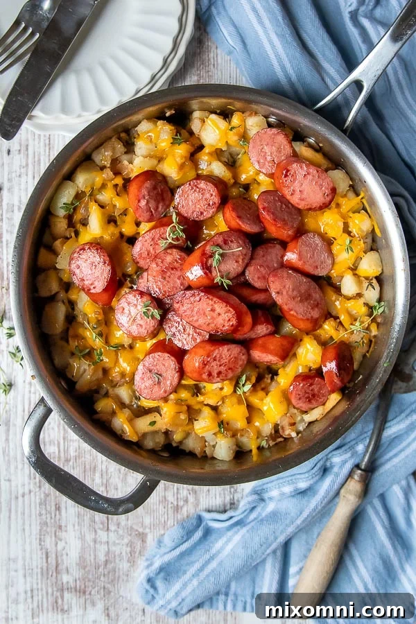 overhead shot of sausage and potatoes in a silver skillet with a blue towel laying next to it
