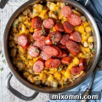 overhead shot of sausage and potatoes in a silver skillet with a blue towel laying next to it