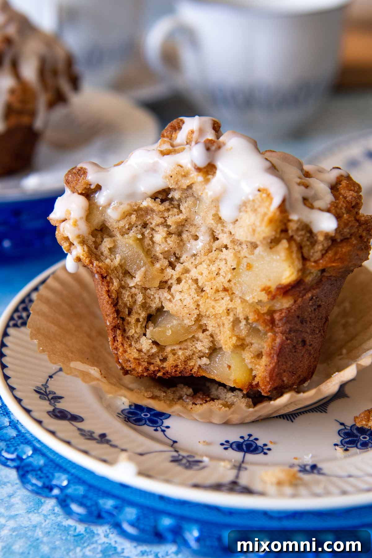 A delicious gluten-free apple muffin on a blue and white plate, with a bite taken out, showcasing the moist interior and crumb topping.