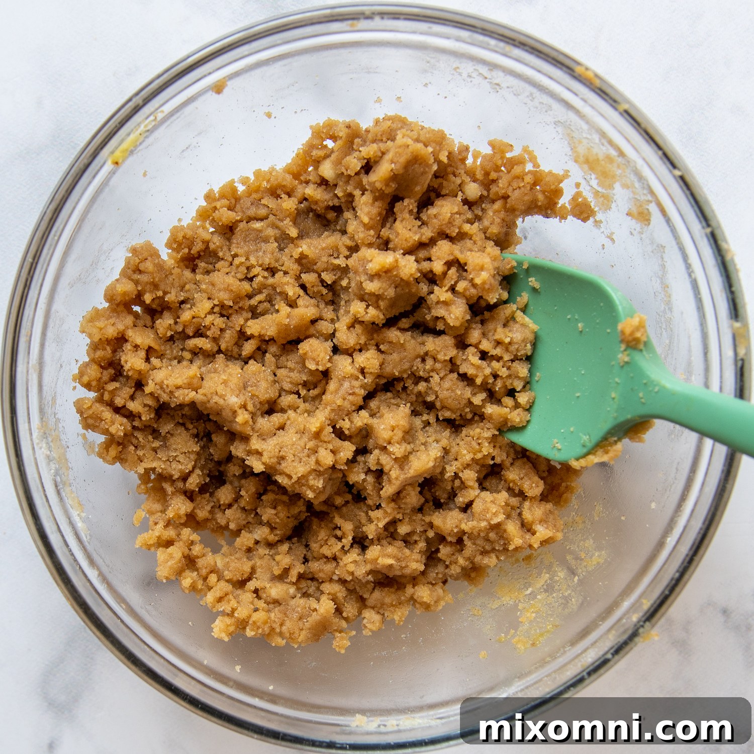 Preparing the crumb topping for apple muffins by mixing dry ingredients with melted butter and egg yolk.