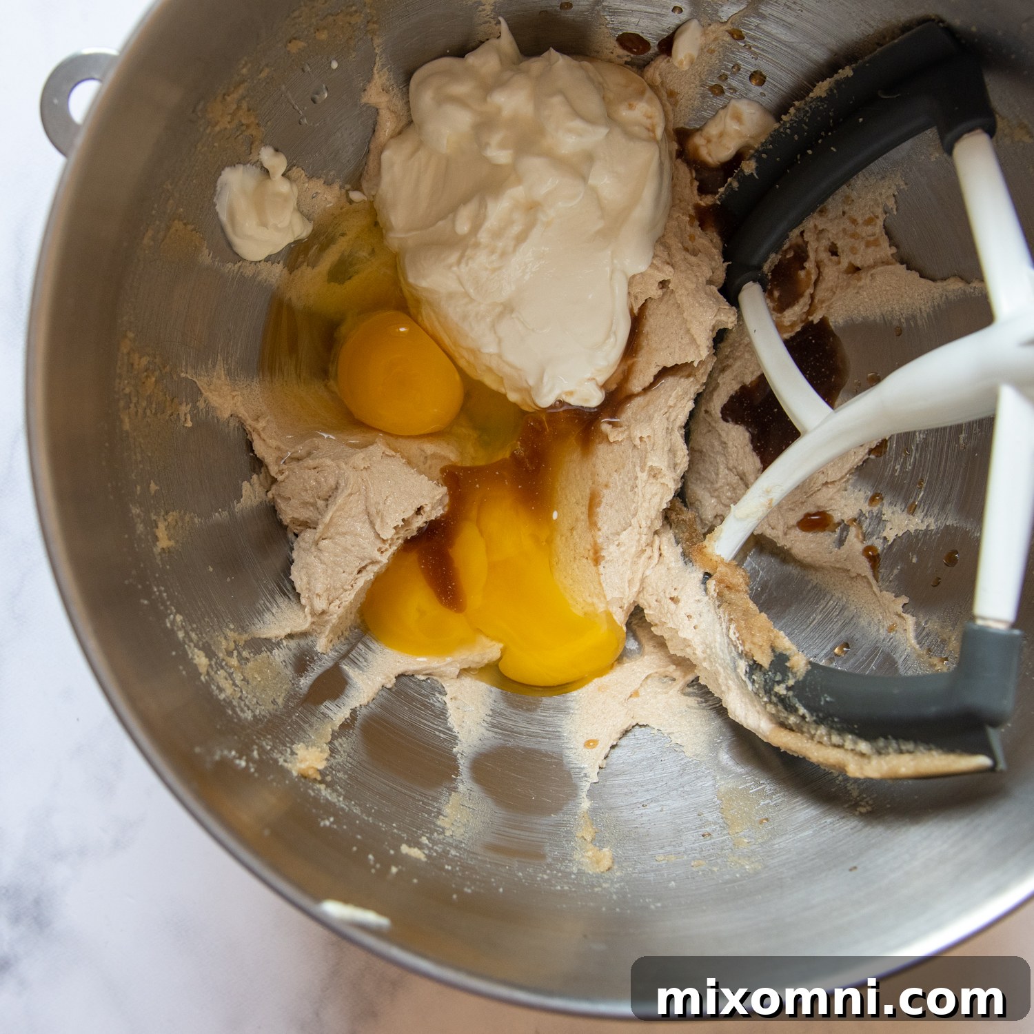 Adding eggs and yogurt to the creamed butter and sugar mixture for the apple muffin batter.
