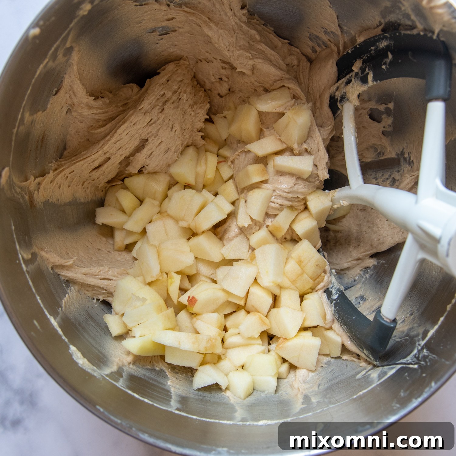 Folding fresh chopped apples into the prepared gluten-free muffin batter.