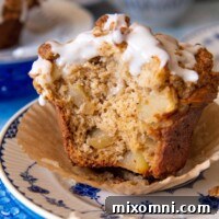 A delicious gluten-free apple muffin on a blue and white plate, with a bite taken out, showcasing the moist interior and crumb topping.