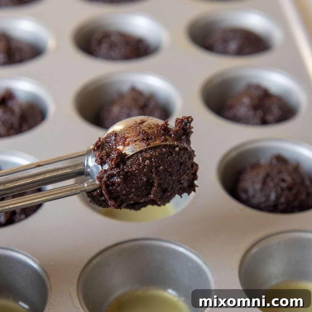 a cookie scoop putting uncooked dough in a mini muffin pan