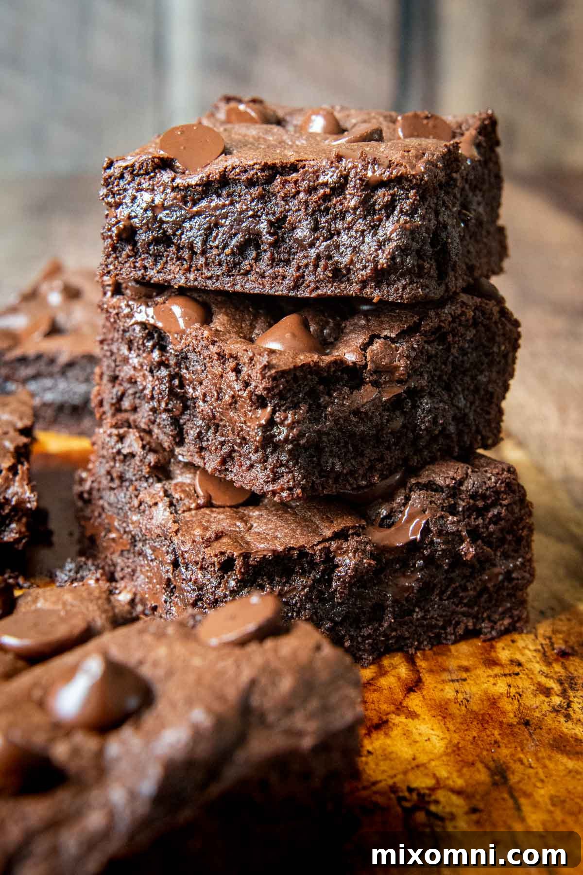 A stack of perfectly fudgy oat flour brownies on a rustic brown cutting board, showcasing their rich texture and delicious appeal.