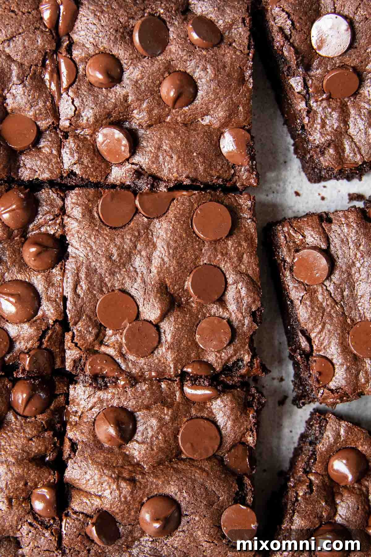 An overhead shot of a pan of freshly baked oat brownies, with melting chocolate chips glistening on top, ready to be sliced.