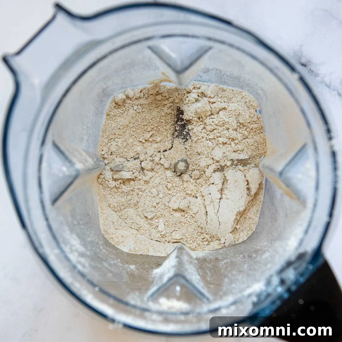 Rolled oats being ground into a fine, powdery oat flour inside a blender.