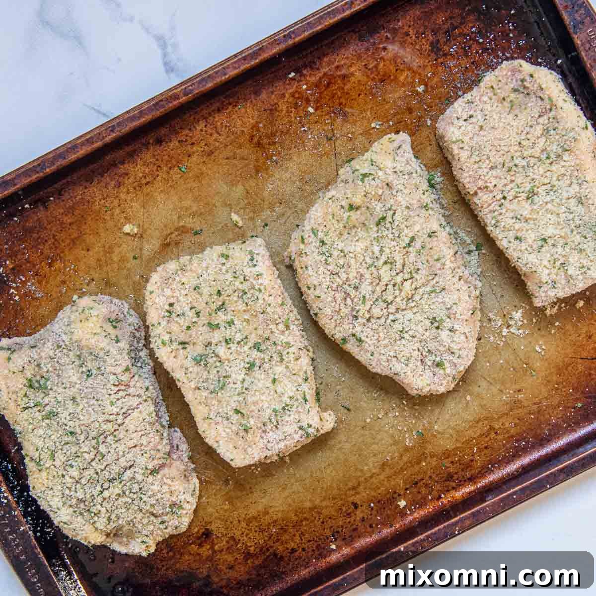 Unbaked breaded pork chops arranged on a preheated baking sheet, ready for the oven.