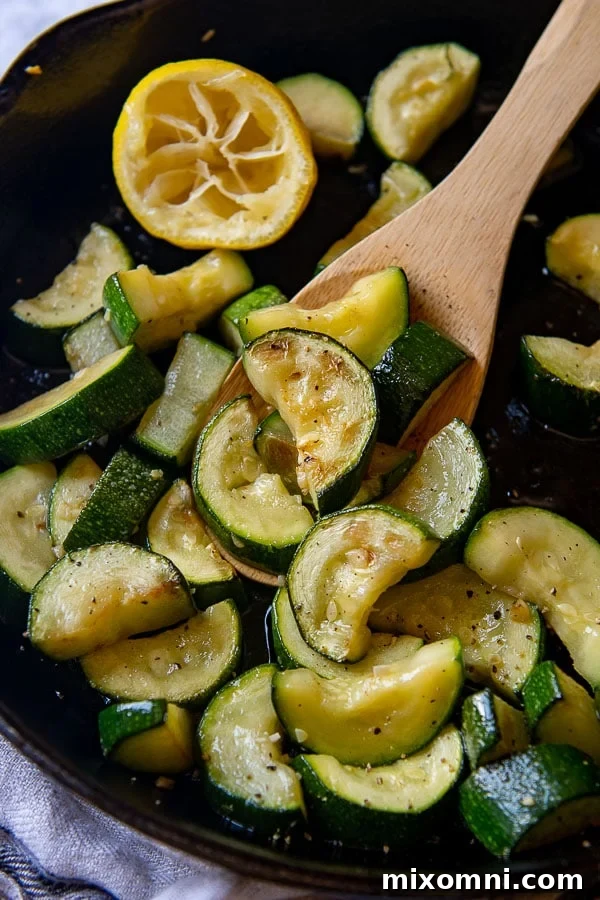 A wooden spoon holding up a serving of freshly cooked sautéed zucchini, garnished with lemon and garlic.