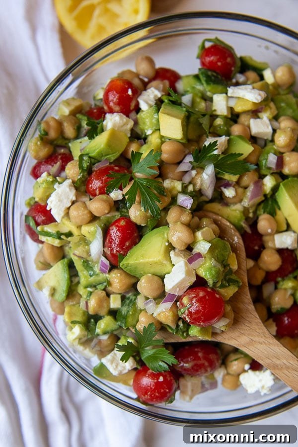 A wooden spoon lifting a spoonful of vibrant Chickpea Avocado Salad, showcasing the colorful ingredients.