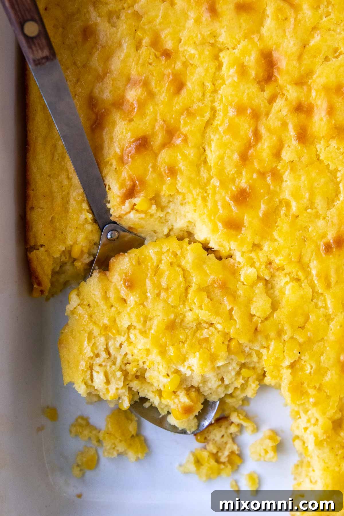 A large serving spoon scooping a portion of warm, fluffy gluten-free corn casserole from a baking dish