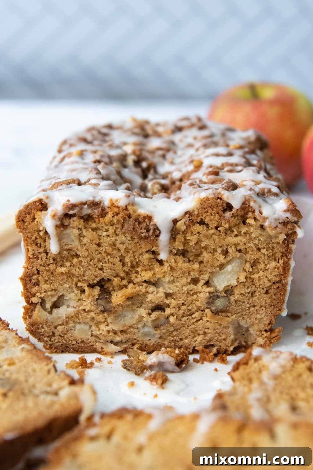 a cut apple bread with apples in the background and frosting dripping down