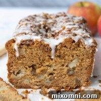 a cut apple bread with apples in the background and frosting dripping down
