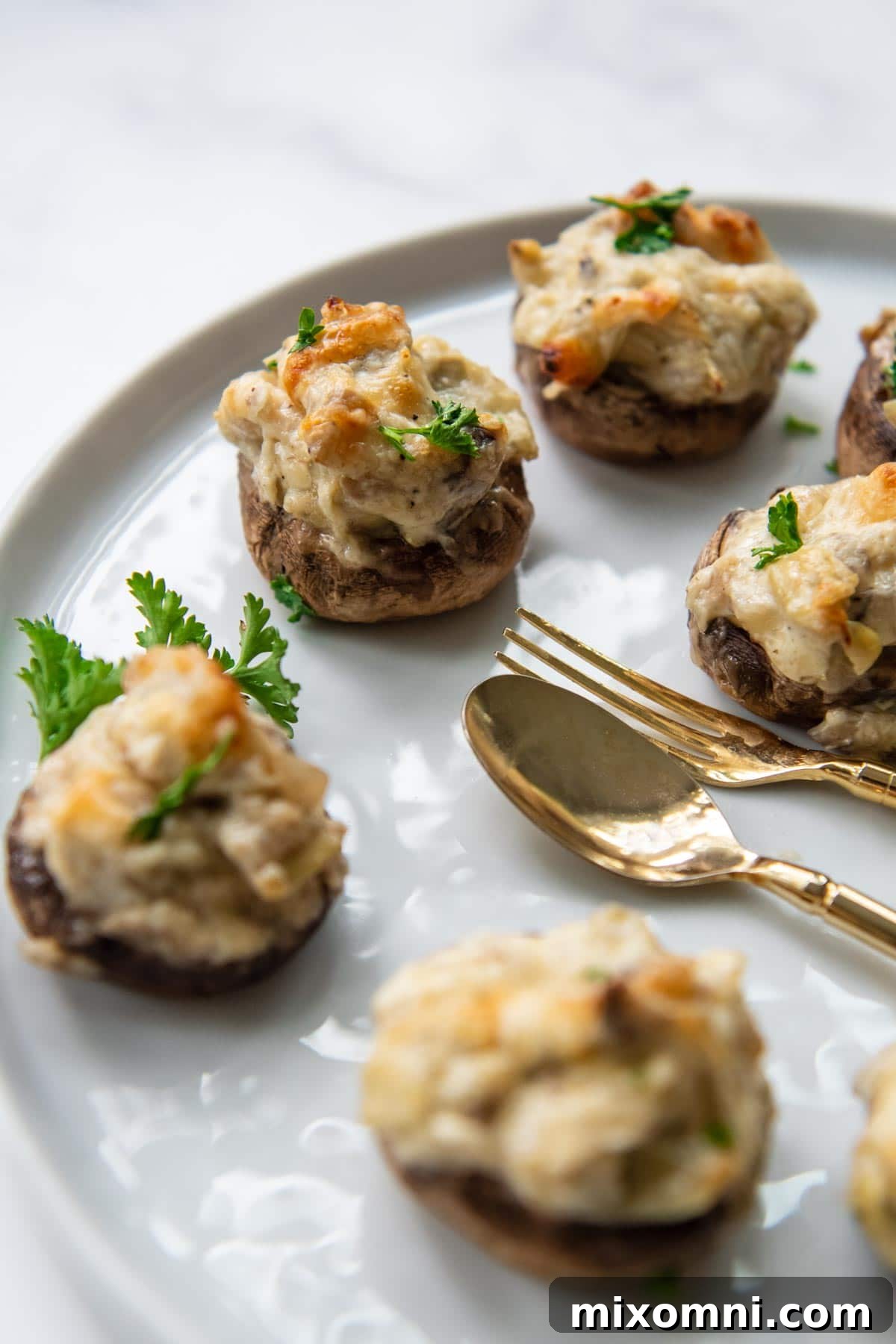 Close-up of golden-brown gluten-free stuffed mushrooms on a white serving platter, garnished with fresh herbs.
