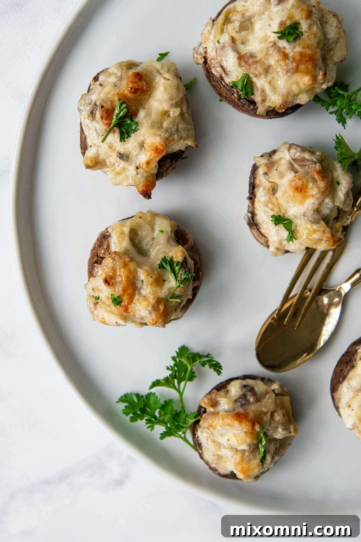 Overhead shot of gluten-free stuffed mushrooms on a white plate with elegant gold serving utensils, ready for a party.