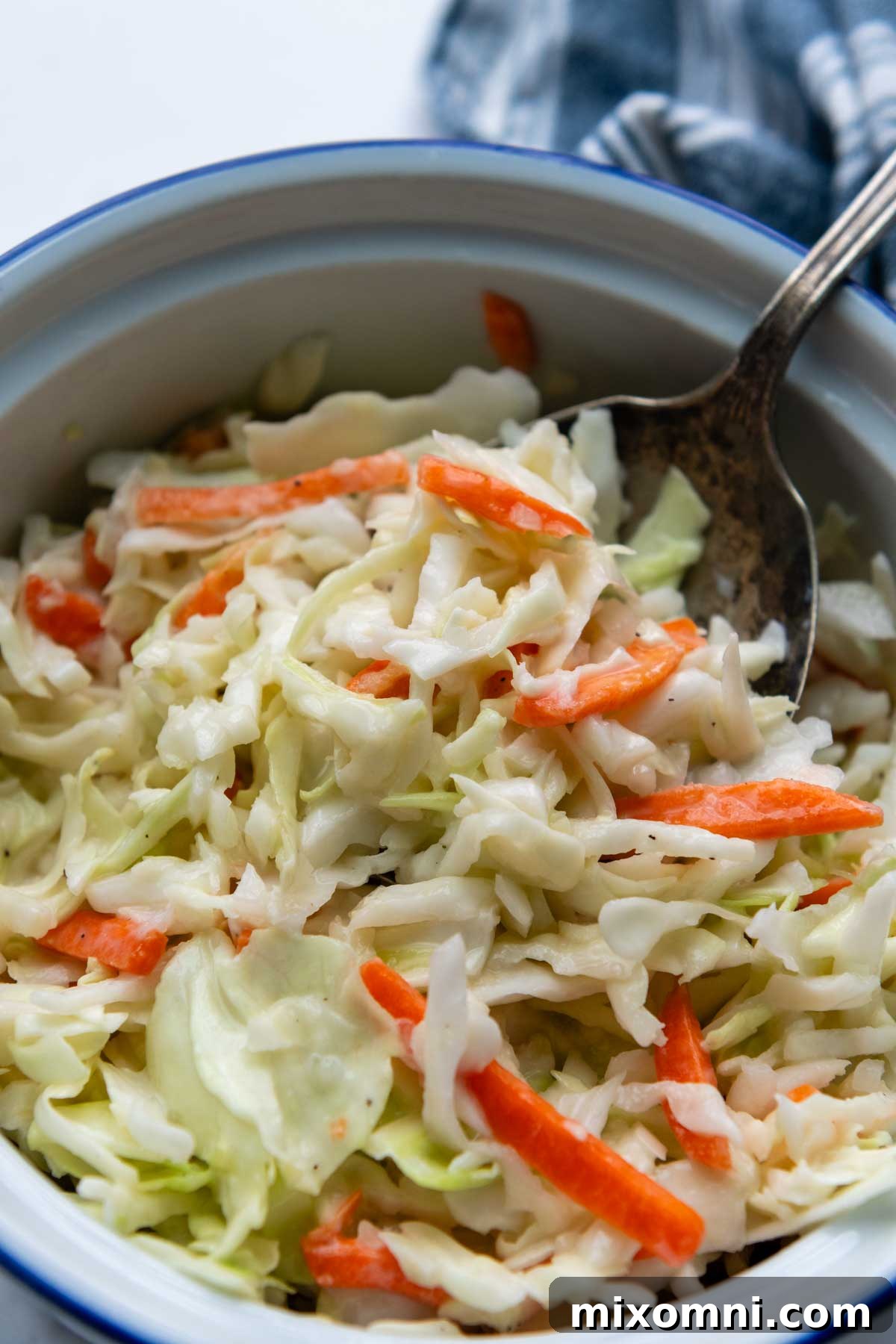 a spoon going into a bowl of coleslaw on a white marble surface.