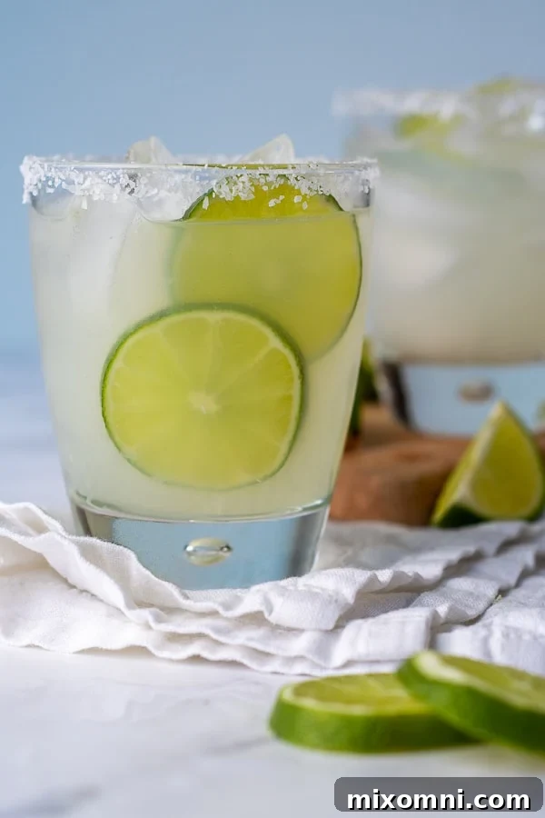 A straight-on shot of a refreshing limeade margarita, garnished with lime slices next to the glass.